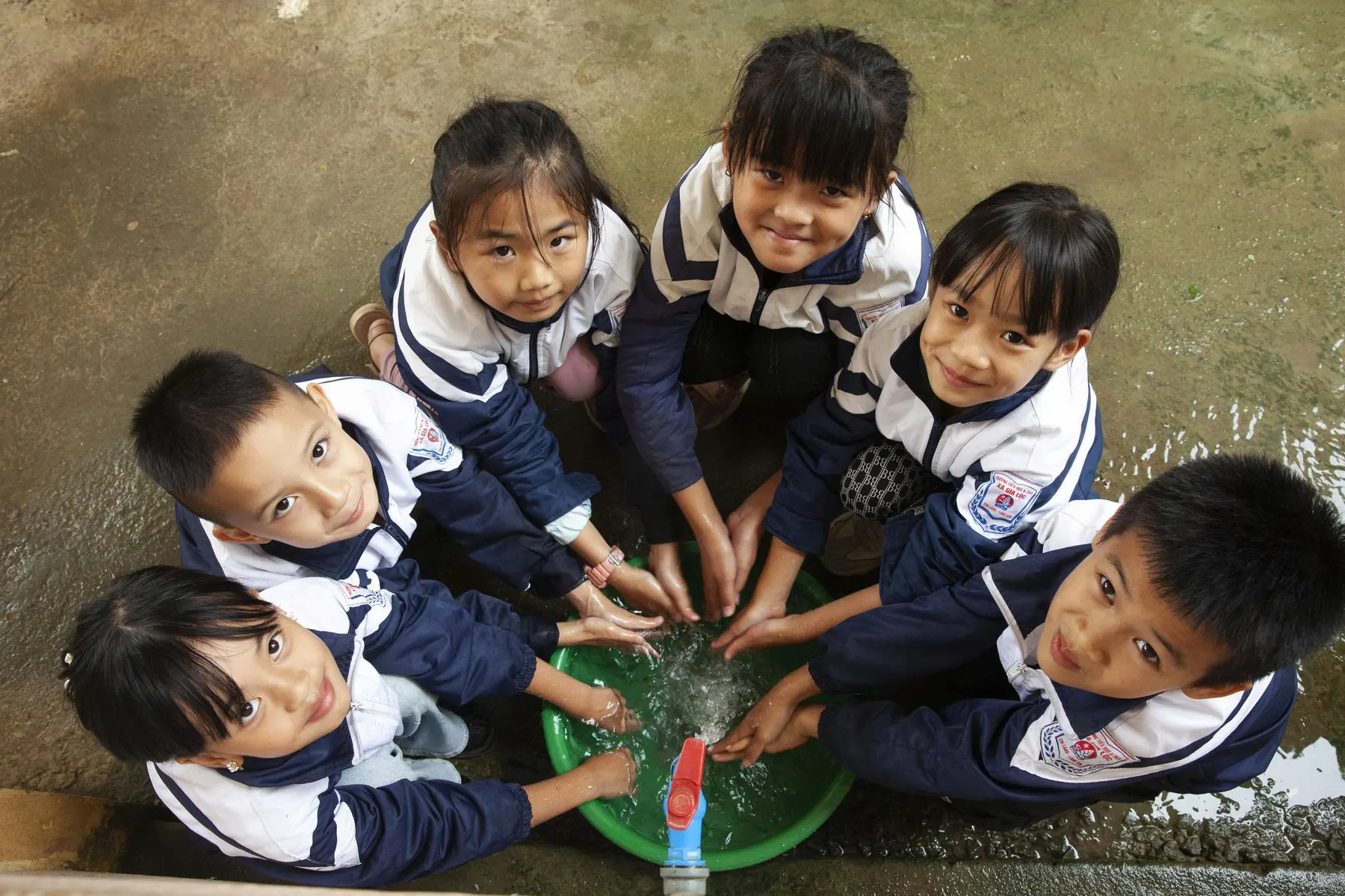 Nhóm học sinh tiểu học vây quanh chậu nước, vừa nghịch nước vừa cười